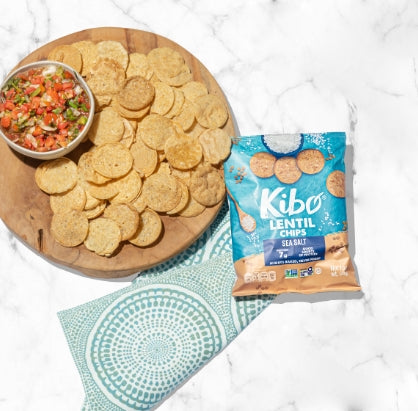 A picture of a plate of Lentil Chips by KIBO, with the bag of chips sitting beside it.